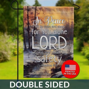 May include: Double-sided garden flag with a serene landscape scene featuring a river and trees. The flag displays the text "In Peace" and a quote from Psalms 4:8. A red circle with the American flag and "Printed in the USA" is visible.
