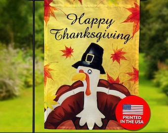 May include: Double-sided Thanksgiving garden flag featuring a cartoon turkey wearing a pilgrim hat. The flag has the words "Happy Thanksgiving" in script, with red and yellow fall leaves on a yellow background. A red circle with the American flag and "Printed in the USA" is on the bottom right.
