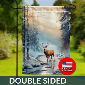 May include: Double-sided garden flag featuring a watercolor painting of a deer in a snowy forest. The flag has a winter landscape with trees and a stream. The flag is printed in the USA.
