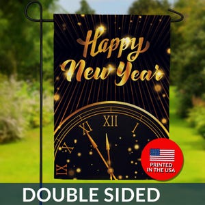 May include: A double-sided garden flag with a black background and gold accents. The flag features the words "Happy New Year" in gold script above a clock face. The clock hands point to midnight. A red circle with the US flag and "Printed in the USA" is on the bottom right.