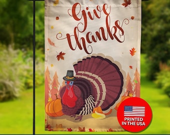 May include: A double-sided garden flag with a Thanksgiving theme. The flag features a cartoon turkey wearing a hat, pumpkins, and the words "Give Thanks" in a decorative font. The flag is printed in the USA.