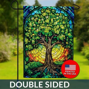 May include: Double-sided garden flag featuring a stained-glass style tree with green leaves, a brown trunk, and roots. The background has a yellow, orange, and blue design. The flag is printed in the USA.