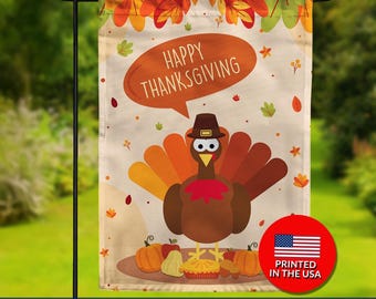 May include: Double-sided Thanksgiving garden flag featuring a cartoon turkey wearing a pilgrim hat and a speech bubble that says "Happy Thanksgiving." The flag has a fall-themed border with leaves and pumpkins.