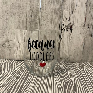 May include: A clear glass wine glass with the text "because toddlers" in black lettering and a small red heart.
