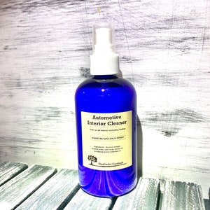 May include: A blue spray bottle with a white label that reads "Automotive Interior Cleaner" and "Shake Before Each Spray". The bottle is sitting on a wooden surface.