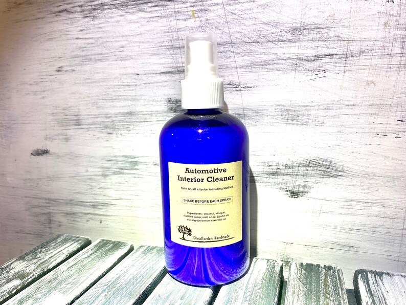 May include: A blue spray bottle with a white label that reads "Automotive Interior Cleaner" and "Shake Before Each Spray". The bottle is sitting on a wooden surface.