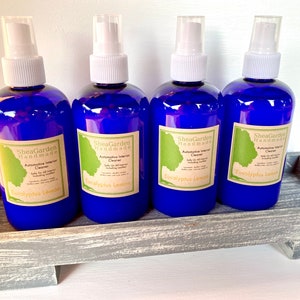 May include: Four blue spray bottles with white tops and labels that say "SheaGarden Handmade" and "Automotive Interior Cleaner" with the scent "Eucalyptus Lemon" on a grey wooden tray.