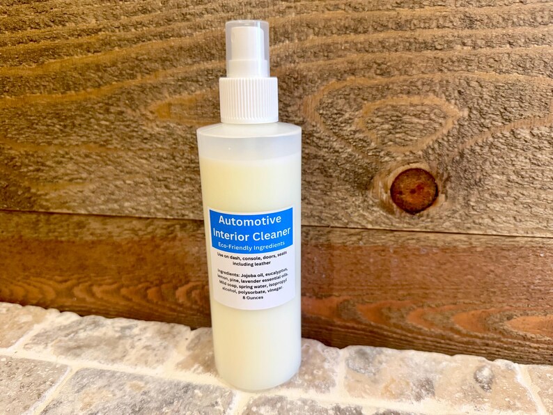 May include: A clear plastic bottle with a white pump top and a blue label that reads "Automotive Interior Cleaner - Eco-Friendly Ingredients". The bottle is filled with a white liquid and is sitting on a wooden surface.