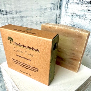 May include: A brown cardboard box with a green label that reads "SheaGarden Handmade Cedar Tree Handmade Soap Bar" and "Net Wt 3.5 OZ". The box contains a bar of brown soap.