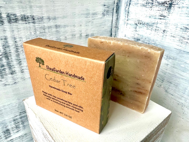 May include: A brown cardboard box with a green label that reads "SheaGarden Handmade Cedar Tree Handmade Soap Bar" and "Net Wt 3.5 OZ". The box contains a bar of brown soap.