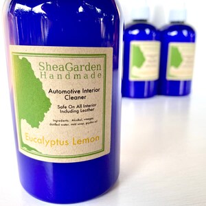 May include: A blue bottle with a brown label that reads "SheaGarden Handmade Automotive Interior Cleaner Safe On All Interior Including Leather Ingredients. Alcohol, vinegar, distilled water, mild soap, jojoba oil Eucalyptus Lemon"