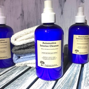 May include: Three blue spray bottles with white spray tops and labels that read "Automotive Interior Cleaner". The bottles are on a whitewashed wooden surface with a stack of towels behind the centre bottle.