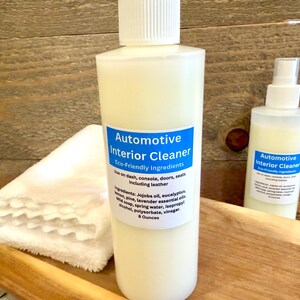 May include: Two bottles of automotive interior cleaner with a blue label that says "Automotive Interior Cleaner" and "Eco-Friendly Ingredients". The bottles are on a wooden surface with white cloths.