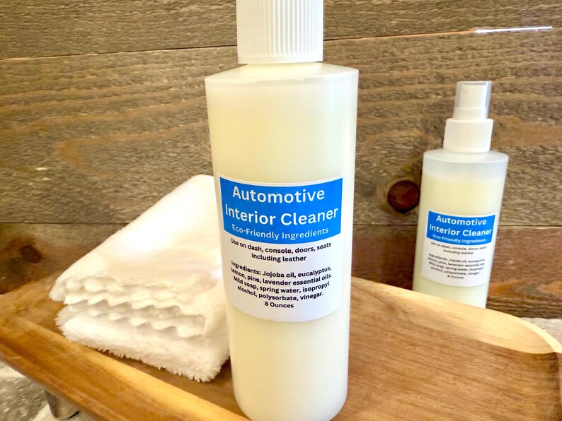 May include: Two bottles of automotive interior cleaner with a blue label that says "Automotive Interior Cleaner" and "Eco-Friendly Ingredients". The bottles are on a wooden surface with white cloths.