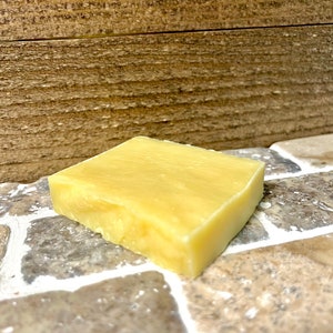 May include: A rectangular bar of pale yellow soap, likely handmade, resting on a tiled surface.
