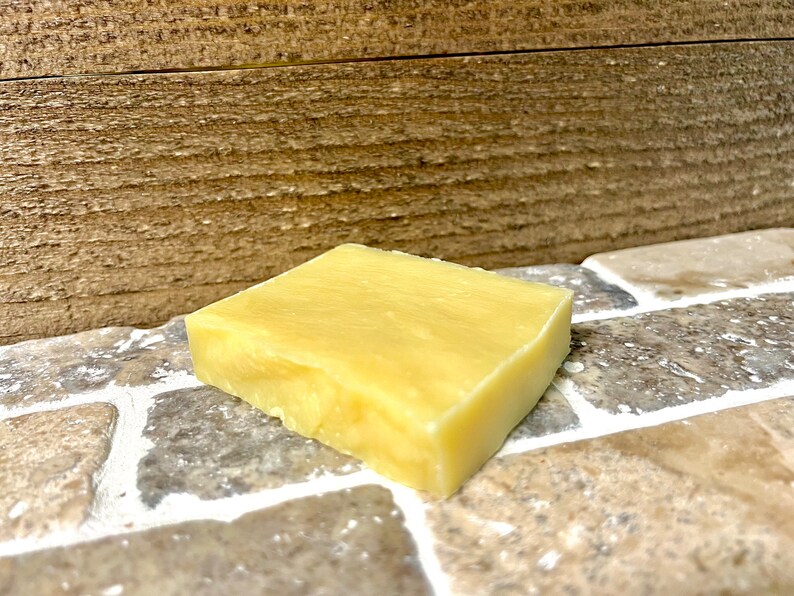 May include: A rectangular bar of pale yellow soap, likely handmade, resting on a tiled surface.
