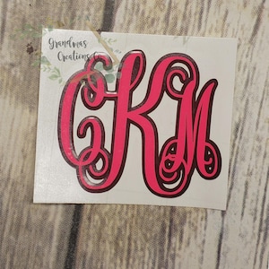 May include: A pink monogram sticker with the letters CKM in a decorative font. The sticker has a black outline and the text "Grandmas Creations" in the upper left corner.