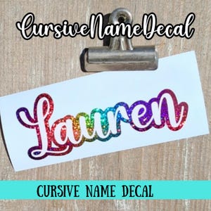 May include: A white decal with the name "Lauren" in a rainbow glitter cursive font. The decal is held by a silver clip. The text "Cursive Name Decal" is at the bottom.