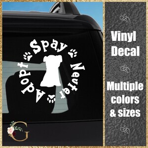 May include: White vinyl decal with a dog silhouette, paw prints, and the words "Adopt, Spay, Neuter." The decal is displayed on a car window. The text "Vinyl Decal, Multiple colors & sizes" is also visible.