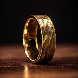 Men's Yellow gold tungsten wedding band with hammered finish standing upright on oak table