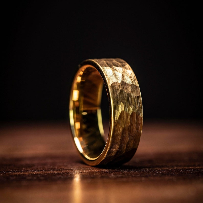Men's Yellow gold tungsten wedding band with hammered finish standing upright on oak table