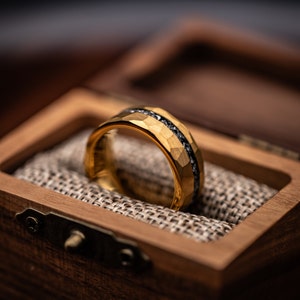 Gold Tungsten wedding band with hammered finish and meteorite inlay in walnut ring box between burlap cushion