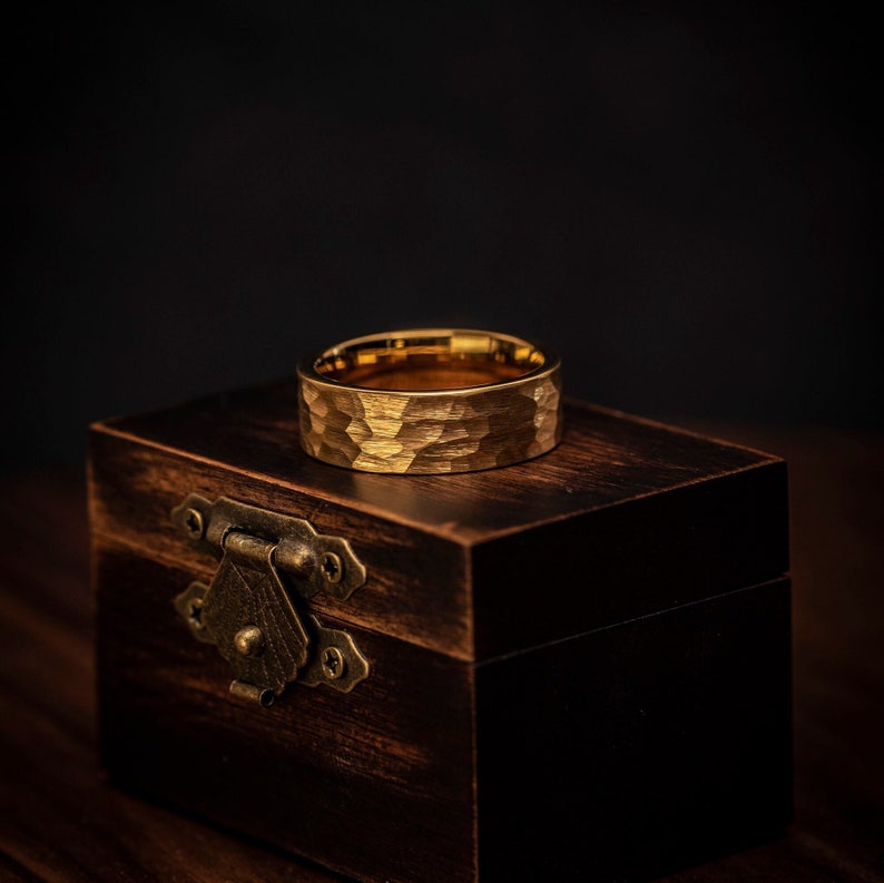 8mm width hammered yellow gold tungsten ring laying on its side on top of walnut ring box