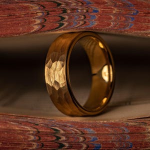 Yellow gold tungsten wedding band with hammered finish standing upright between book pages