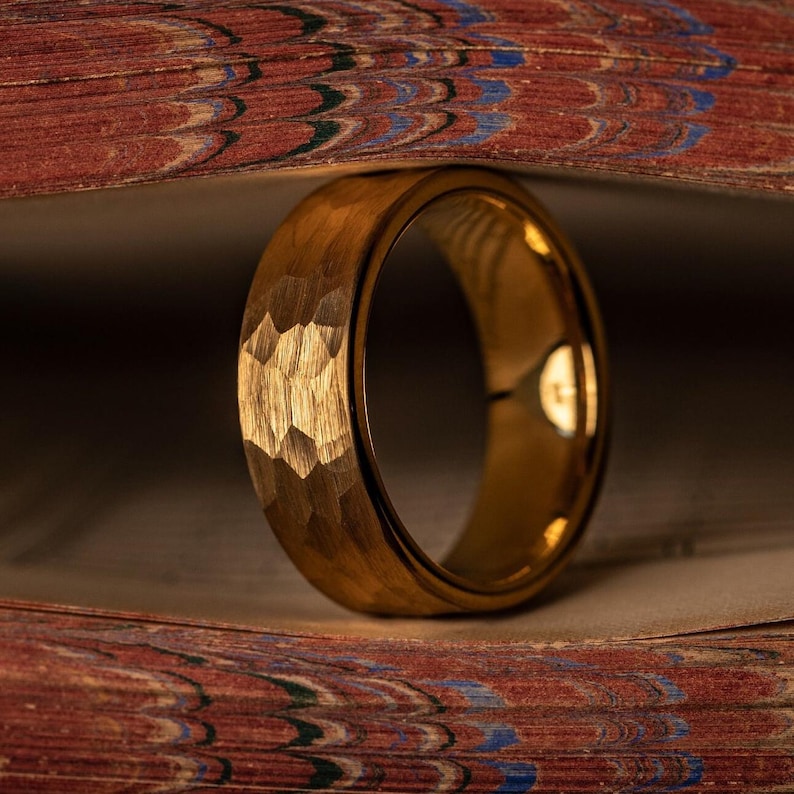 Yellow gold tungsten wedding band with hammered finish standing upright between book pages