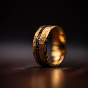 Men's Tungsten wedding ring with gold plating and hammered finish including meteorite inlay standing upright on oak table