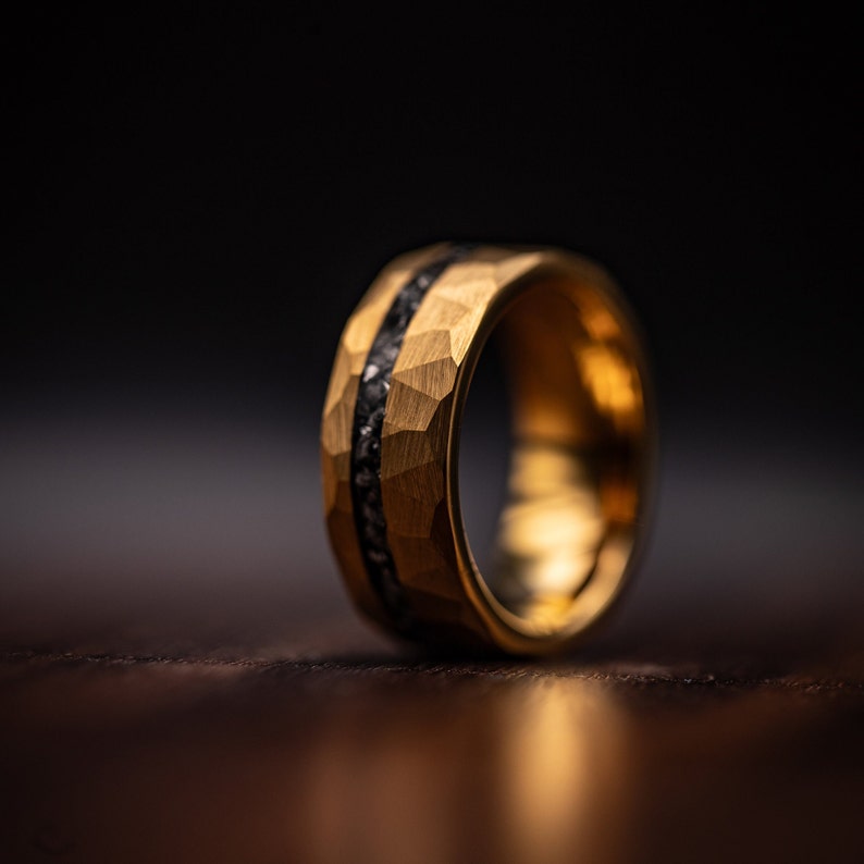 Men's Tungsten wedding ring with gold plating and hammered finish including meteorite inlay standing upright on oak table