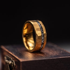 8mm Yellow gold tungsten wedding band with hammered finish and meteorite inlay standing upright on walnut ring box