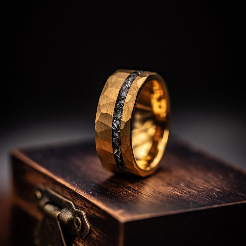 Men's Gold hammered wedding ring with silver meteorite inlay standing upright on walnut ring box