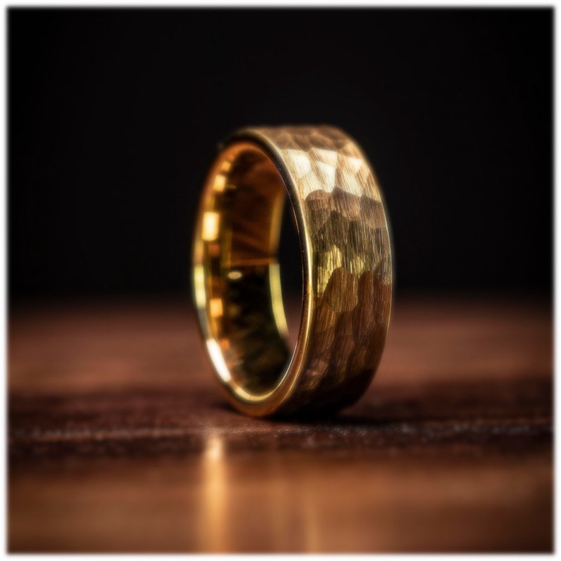 18k yellow gold tungsten wedding ring with hammered finish standing upright on oak table