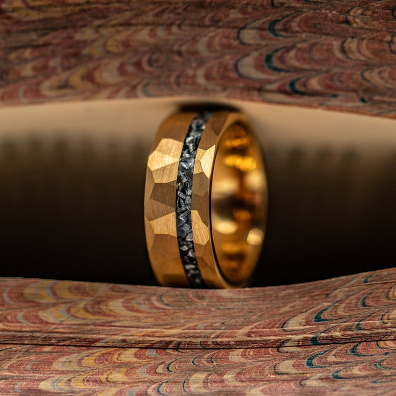 Hammered Gold tungsten wedding band with silver meteorite channel standing upright between book pages