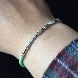 May include: A silver bracelet with small round beads and silver bars. The bracelet is on a person's wrist.