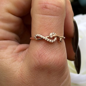 May include: A gold ring with a delicate infinity symbol design, accented with small sparkling stones. The ring is worn on a finger.