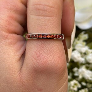 May include: A silver band ring with a row of small, red gemstones.