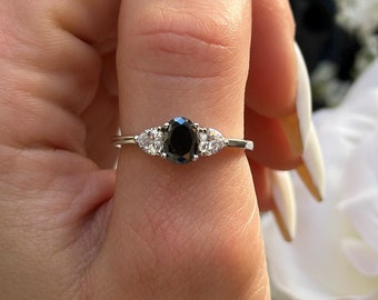 May include: A silver ring with a black oval-shaped gemstone and two smaller white gemstones on either side.
