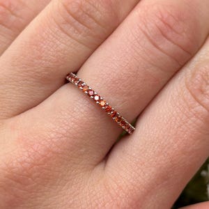 May include: A delicate eternity band ring with a row of small, sparkling red gemstones.