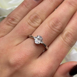 May include: A silver ring with an oval-shaped clear gemstone and two smaller clear gemstones on either side.