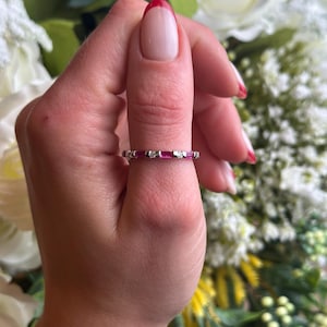 May include: A delicate eternity band ring with alternating red ruby and clear diamond stones set in a white gold band.