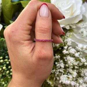 May include: A delicate eternity band ring with a row of small pink gemstones set in a thin gold band.