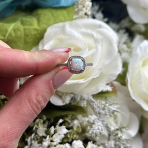 May include: A silver ring with a white opal gemstone surrounded by a halo of smaller clear gemstones.