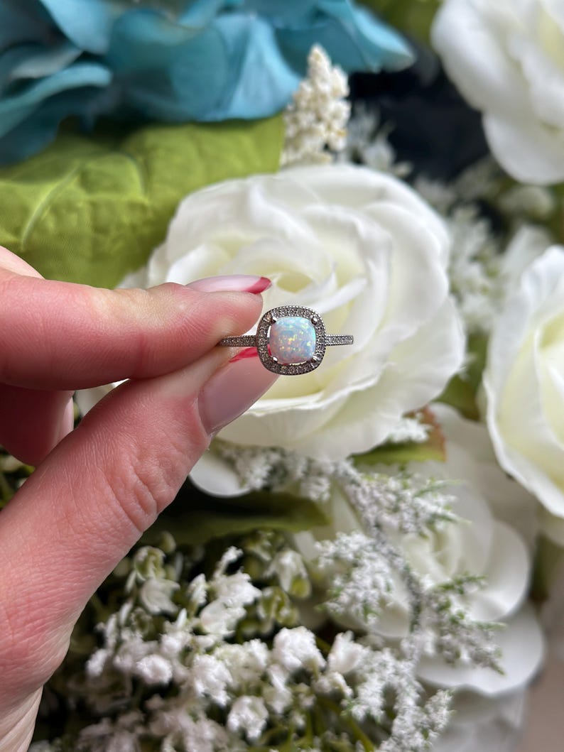 May include: A silver ring with a white opal gemstone surrounded by a halo of smaller clear gemstones.