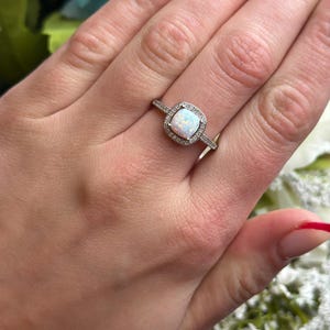 May include: A silver ring with a white opal gemstone surrounded by smaller clear gemstones.