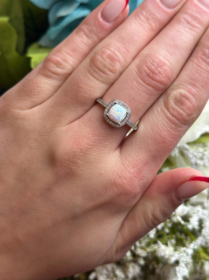 May include: A silver ring with a white opal gemstone surrounded by smaller clear gemstones.