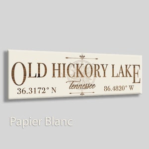 May include: A white wooden sign with brown text that reads "Old Hickory Lake" with a compass graphic and the coordinates "36.3172° N" and "86.4820° W". The text "Tennessee" is also included on the sign.