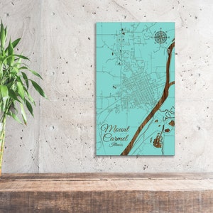 May include: A teal blue wooden map of Mount Carmel, Illinois. The map is laser cut and features a compass rose and the city name in brown text.