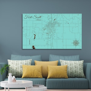 May include: A teal blue wooden map of Fort Scott, Kansas. The map features a compass rose and the city's name in a brown font.